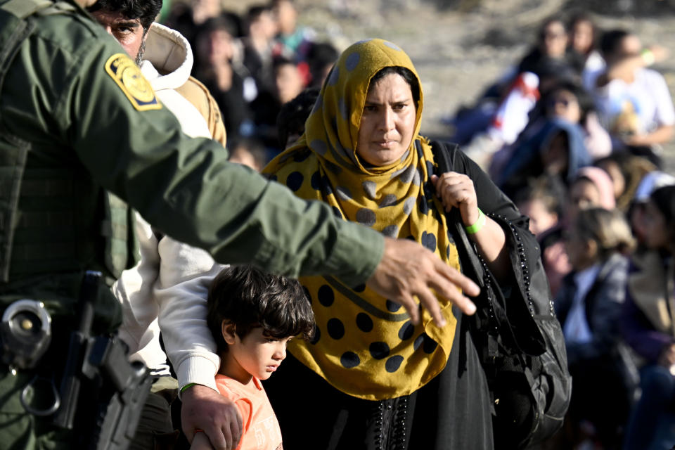 FILE - An asylum-seeker carries her baby past U.S. Border Patrol agents as they wait between the double fence along the U.S.-Mexico border near Tijuana, Mexico, Monday, May 8, 2023, in San Diego. As President Joe Biden's administration prepares for the end of asylum restrictions related to the COVID-19 pandemic, it is offering some new legal options for people — especially families — to come to the United States. The administration said it will admit at least 100,000 Latin Americans seeking to reunite with family members in the United States, but has released almost no details. (AP Photo/Denis Poroy, File)