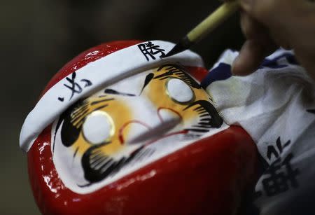 Japanese craftsman Sumikazu Nakata writes the Chinese character of "victory", which is a part of the phrase "Certain victory", as he adds the final touches on a Daruma doll, which is believed to bring good luck, at his studio "Daimonya" in Takasaki, northwest of Tokyo November 23, 2014. REUTERS/Yuya Shino