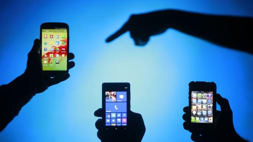 Men are silhouetted against a video screen as they pose with Samsung Galaxy S3, Nokia Lumia 820 and iPhone 4 smartphones (L-R) in this photo illustration taken in the central Bosnian town of Zenica, May 17, 2013. REUTERS/Dado Ruvic (BOSNIA AND HERZEGOVINA - Tags: BUSINESS TELECOMS) - RTXZQ6G