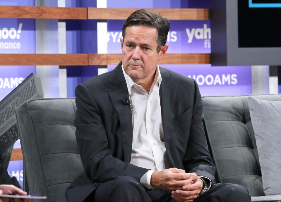 A man in a suit sits on a stage with "Yahoo!" behind him.