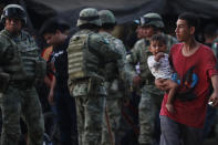 Un hombre lleva a su hijo en brazos junto a varios guardias nacionales mexicanos, en la orilla mexicana del río Suchiate, en la frontera con Guatemala, cerca de Ciudad Hidalgo, en Mëxico, el lunes 20 de enero de 2020. (AP Foto/Marco Ugarte)