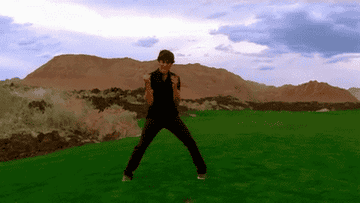 Zac Efron in a desert landscape dancing passionately with mountains in the background