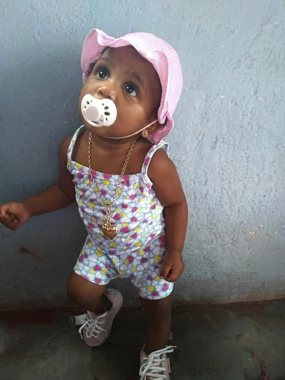 In this Feb. 10, 2020, photo, provided by Andréa de Sousa, her daughter Vitoria Gabrielle looks up while leaning against a wall, in Rio de Janeiro, Brazil. The girl with a constant smile celebrated her first birthday in February, but after recovering from viral meningitis, Vitoria Gabrielle suffered gastrointestinal problems that sent her from her mother's barely furnished hilltop home back to the hospital several times for treatment. It was during an April hospital stay that de Sousa suspects her daughter was infected with the coronavirus that was just starting to circulate in Rio and Brazil. Vitoria Gabrielle died in June. (Courtesy of Andréa de Sousa via AP)