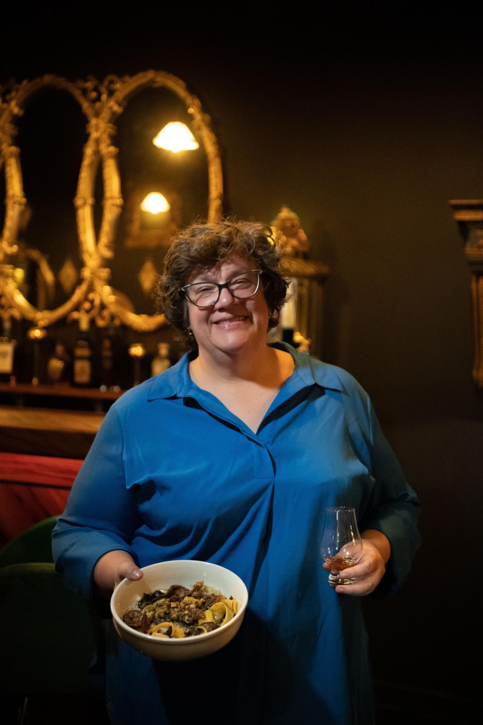 Tamara Gnyp, owner of the Italian restaurant, Trattoria La Caverna in Hendersonville, Tenn., Friday, Feb. 23, 2024 holds up a glass of bourbon and the Pappardelle ai Funghi. Her restaurant once served a Thai food until she became deadly allergic to lemongrass, a popular ingredient in Thai cooking.