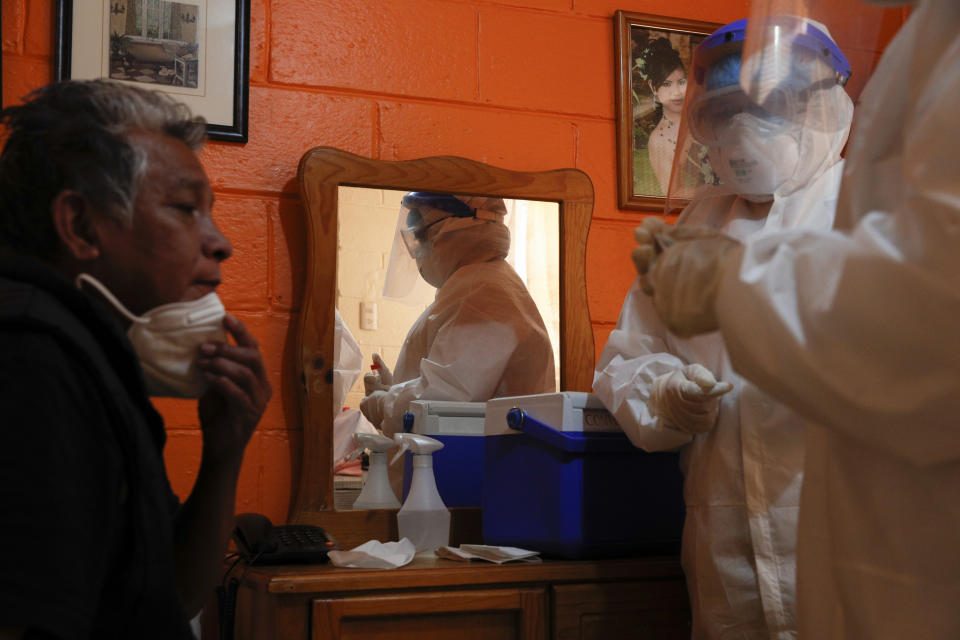 Ricardo Leon Luna, 74, lowers his mask as Doctors Delia Caudillo, right, and Monserrat Castaneda, prepare to take throat and nasal swabs as they conduct a COVID-19 test in his home in the Venustiano Carranza borough of Mexico City, Thursday, Nov. 19, 2020. (AP Photo/Rebecca Blackwell)