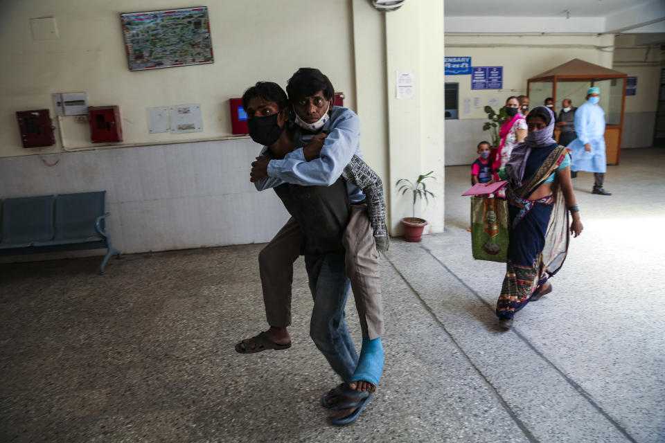 A man carries another on his back as he brings him for medical check up at a government hospital in Jammu, India, Monday, June 21, 2021. (AP Photo/Channi Anand)