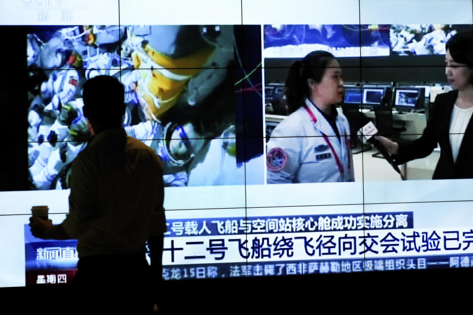 A man is silhouetted as he watches a TV screen showing CCTV broadcasting a news of Chinese astronauts sit inside the Shenzhou-12 manned spacecraft preparing to return to earth, at a shopping mall in Beijing, Thursday, Sept. 16, 2021. (AP Photo/Andy Wong)
