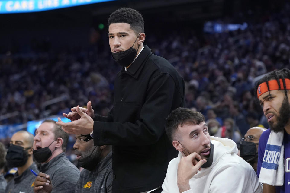 Injured Phoenix Suns guard Devin Booker applauds from the bench during the first half of the team's NBA basketball game against the Golden State Warriors in San Francisco, Friday, Dec. 3, 2021. (AP Photo/Jeff Chiu)