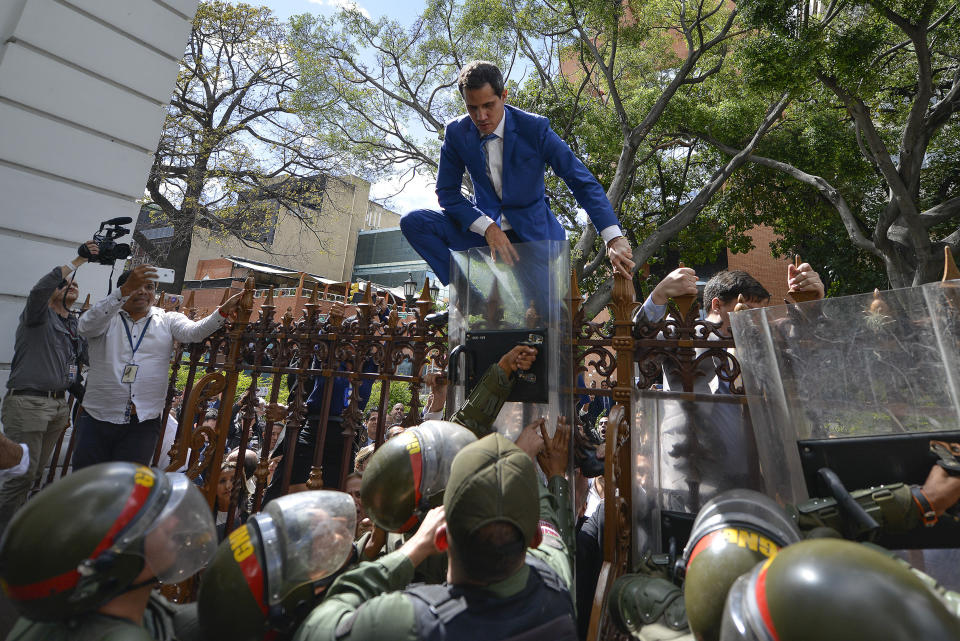 National Assembly President Juan Guaido, Venezuela's opposition leader, climbs the fence in a failed attempt to enter the Assembly compound as he and other opposition lawmakers are blocked from entering a session to elect the body's new leadership in Caracas, Venezuela, Sunday, Jan. 5, 2020. (AP Photo/Matias Delacroix)