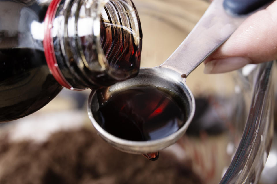 A close-up of vanilla extract being poured into a teaspoon, in preparation for mixing with another ingredient