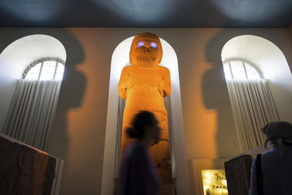 Visitors pass the Statue of Hadad, the Weather God, illuminated by artist Liam Gillick during a press preview for his exhibition Filtered Time at Pergamon Museum in Berlin, Tuesday, April 4, 2023. A new light and sound installation by British contemporary artist Liam Gillick, part of the show Filtered Time, opened Tuesday at one of the German capital's most popular museums. (AP Photo/Stefanie Loos)