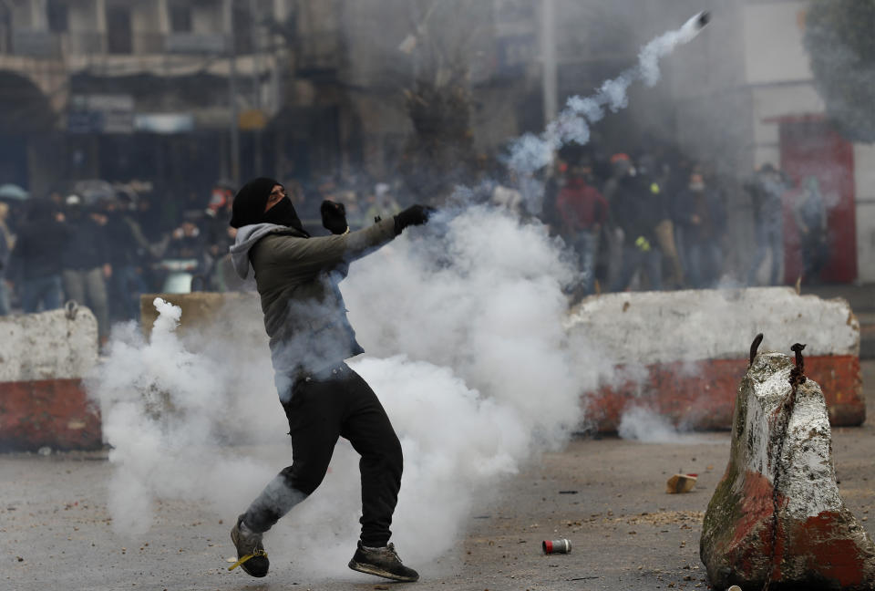 A protester throws back a tear gas canister towards riot policemen during a protest against deteriorating living conditions and strict coronavirus lockdown measures, in Tripoli, north Lebanon, Thursday, Jan. 28, 2021. Violent confrontations between protesters and security forces over the last three days in northern Lebanon left a 30-year-old man dead and more than 220 people injured, the state news agency said Thursday. (AP Photo/Hussein Malla)