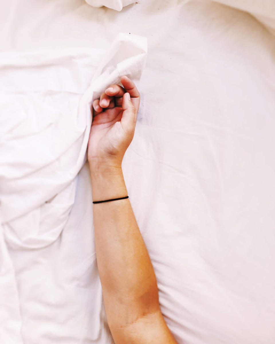 Person's arm gripping a white sheet, partially covered, evoking a waking-up scene