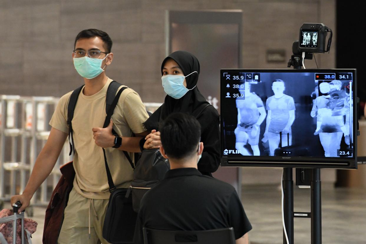 A couple, wearing protective facemasks amid fears about the spread of the COVID-19 novel coronavirus, walk past a temperature screening check at Changi International Airport in Singapore on February 27, 2020. (Photo by Roslan RAHMAN / AFP) (Photo by ROSLAN RAHMAN/AFP via Getty Images)