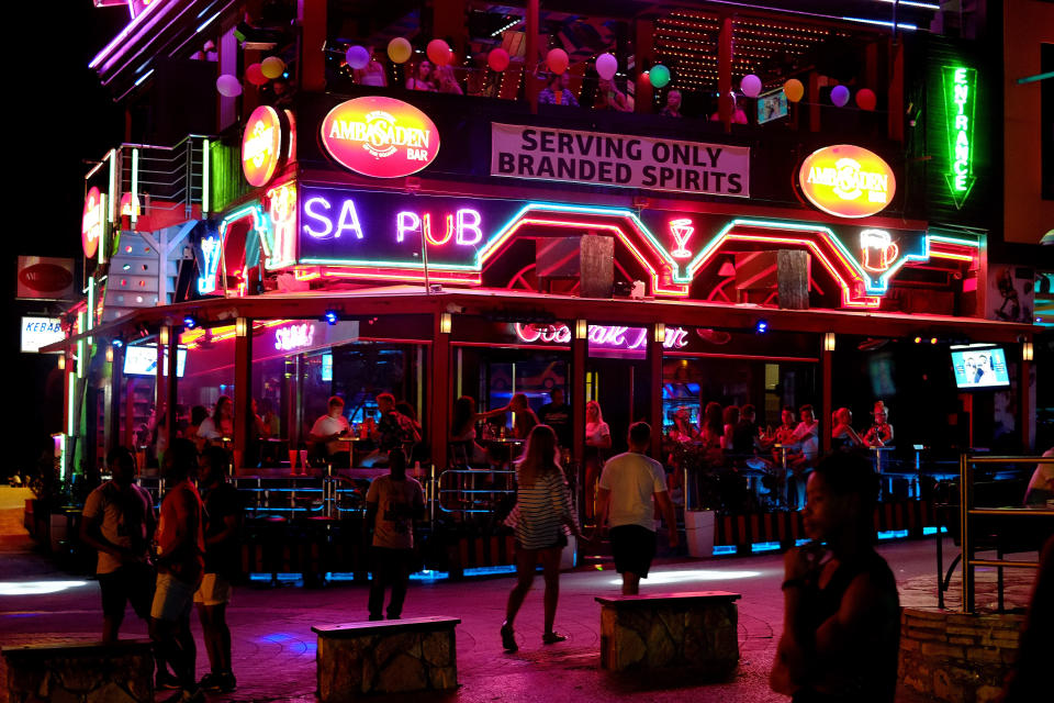 Tourist enjoy their drinks in a pub as other walk in southeast resort of Ayia Napa in the east Mediterranean island of Cyprus late Wednesday, July 17, 2019. A Cyprus police official says 12 Israelis have been detained after a 19-year-old British woman alleged that she was raped in the resort town of Ayia Napa. (AP Photo/Petros Karadjias)