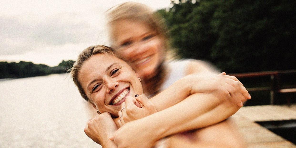 two white women laughing on a beach one has their face blurred and arms around the woman who is clearly in focus