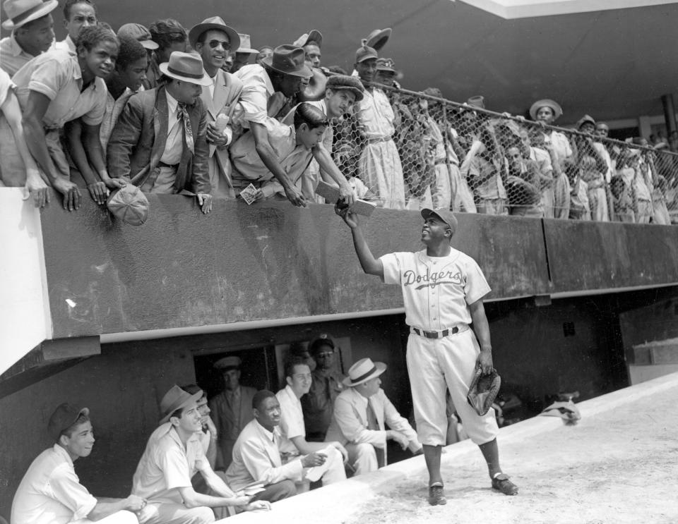 FILE - In this March 6, 1948, file photo, Jackie Robinson, first baseman of the Brooklyn Dodgers, returns an autograph book to a fan in the stands, during the Dodgers' spring training in Ciudad Trujillo, now Santo Domingo, in the Dominican Republic. Baseball holds tributes across the country on Jackie Robinson Day, Tuesday, April 15, 2014, the 67th anniversary marking the end of the game's racial barrier. (AP Photo/File)