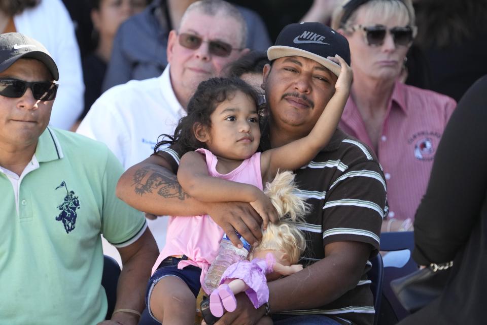 Mass shooting survivor Wilson Garcia holds a young girl during a vigil for his son, Daniel Enrique Laso, Sunday, April 30, 2023, in Cleveland, Texas. Garcia's son and wife were killed in the shooting Friday night. The search for a Texas man who allegedly shot his neighbors after they asked him to stop firing off rounds in his yard stretched into a second day Sunday, with authorities saying the man could be anywhere by now. The suspect fled after the shooting Friday night that left multiple people dead, including the young boy. (AP Photo/David J. Phillip)