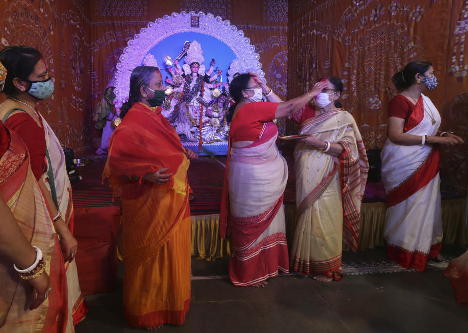 A devotee applies vermilion on the face of another during Durga Puja festival in Mumbai, India, Monday, Oct. 26, 2020. The Hindu festival season is traditionally laced with an unmatched fanfare and extravaganza, with socializing being the hallmark of the celebration. But because of the coronavirus pandemic this year's festivities have started on a pale note. (AP Photo/Rafiq Maqbool)