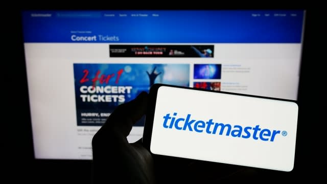 A person holds a phone up with the Ticketmaster logo in front of a computer.