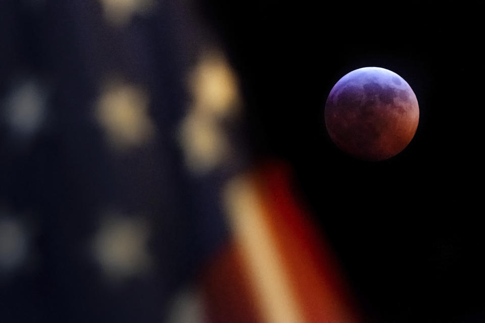 A U.S. Flag in downtown Washington flies in front of the moon during a lunar eclipse, Sunday, Jan. 20, 2019. The entire eclipse will exceed three hours. Totality - when the moon's completely bathed in Earth's shadow - will last an hour. Expect the eclipsed, or blood moon, to turn red from sunlight scattering off Earth's atmosphere. (AP Photo/J. David Ake)