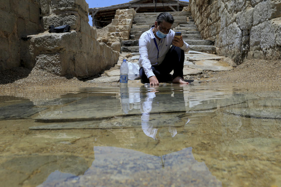 El cristiano sirio Zuhair Al-Sahawi sumerge la mano en agua en el lugar de bautismo Bethany Beyond, en la rivera oriental del río Jordán en Jordania, el miércoles 8 de junio de 2022. (AP Foto/Raad Adayleh)