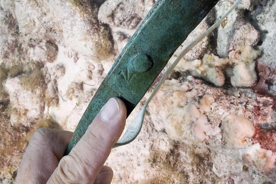 In this undated photo provided by the National Park Service, a diver identifies a "broad arrow" marking on a copper barrel band denoting ownership by the British military during recent archeological survey in Dry Tortugas National Park, Fla. Copper barrel bands were used on small barrels of copper during the 18th century. National Park Service archeologists identified the archeological remains belonging to the HMS Tyger, an 18th century British warship. The Fourth-Rate, 50-gun frigate sunk in 1742 after it ran aground on the reefs of the Dry Tortugas while on patrol in the War of Jenkins Ear between Britain and Spain. While the remains of the historic shipwreck were first located in 1993, new research has uncovered definitive evidence. (Brett Seymour/National Park Service via AP)