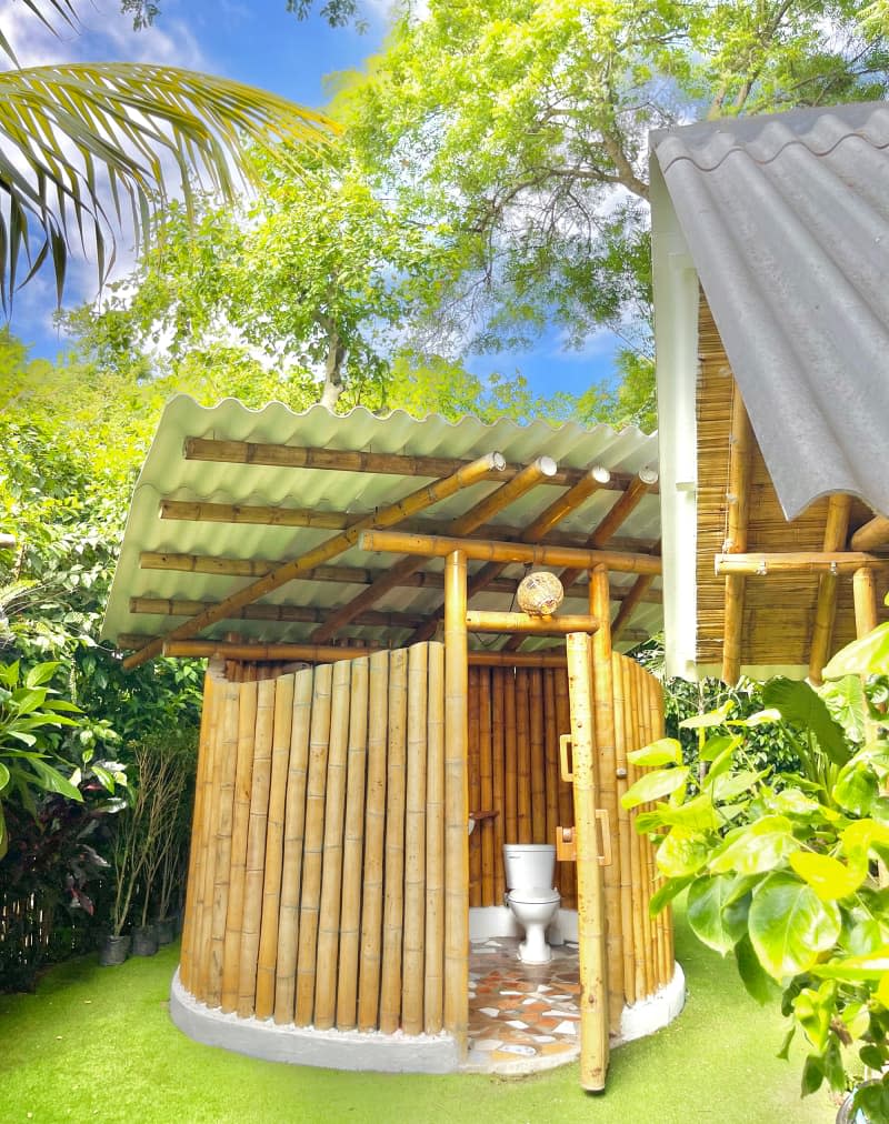 Bathroom in outdoor bamboo structure with metal roof.