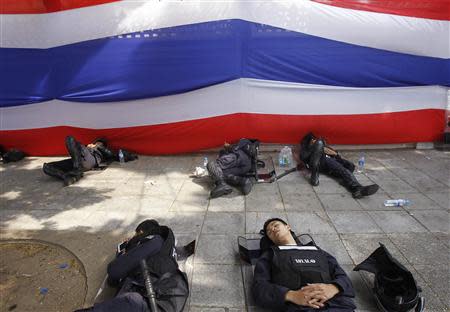 Riot policemen rest near a large Thai national flag outside the Government House in Bangkok December 14, 2013. REUTERS/Chaiwat Subprasom