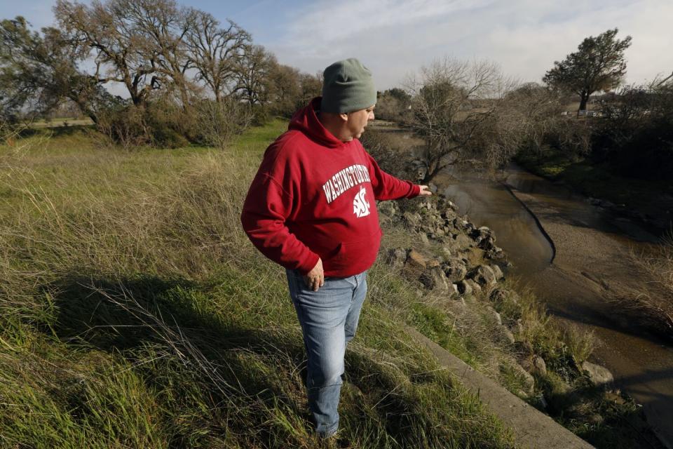 A man stands beside a stream.