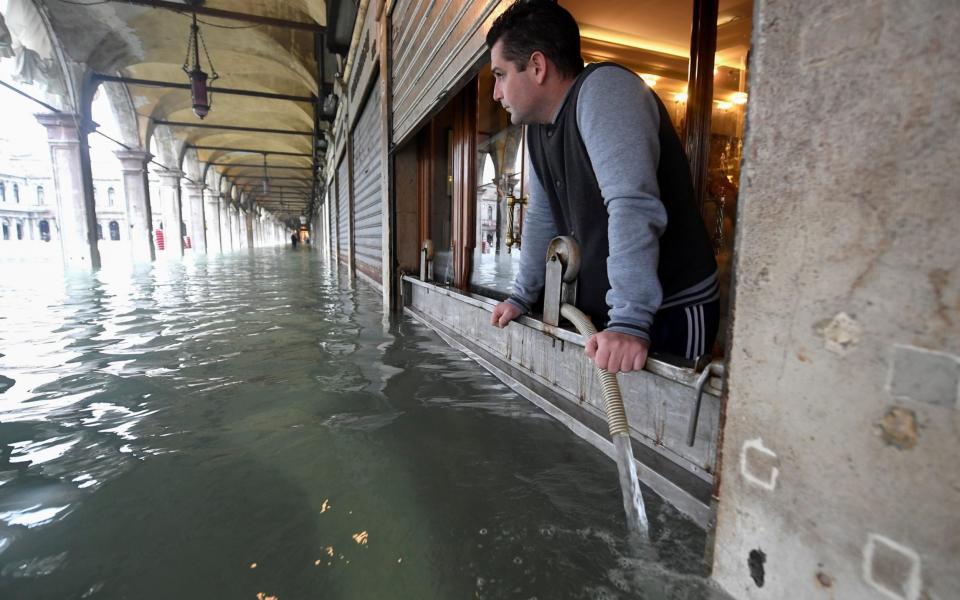 A man pumps water out of a flooded shop in St Mark's Square - Reuters
