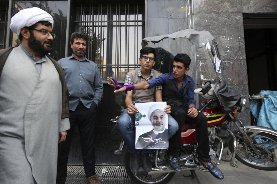 A supporter of Iranian presidential candidate Hassan Rouhani holds his poster as another youth waves to a clergyman outside the campaign headquarters of Rouhani, in Tehran, a day after the election, Iran, Saturday, June 15, 2013. (AP Photo/Vahid Salemi)