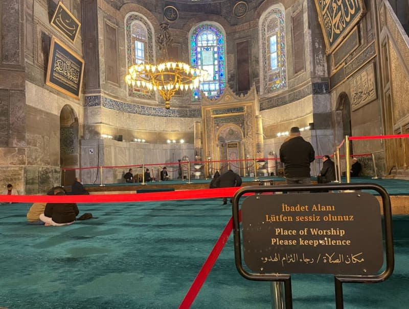 A man prays in front of a barrier in an area reserved for men. Signs point to the quiet area. Linda Say/dpa