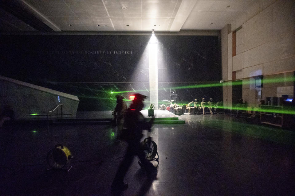 FILE - In this July 24, 2020, file photo, green lines cast by protesters' laser pointers cross the darkened lobby of the Mark O. Hatfield U.S. Courthouse as federal officers wait for a possible skirmish with demonstrators in Portland, Ore. An Associated Press analysis of more than 200 arrests shows that even those accused of breaking the law during the nightly rallies don’t neatly fit into President Donald Trump’s depiction of protesters as “anarchists and agitators.” (AP Photo/Noah Berger, File)