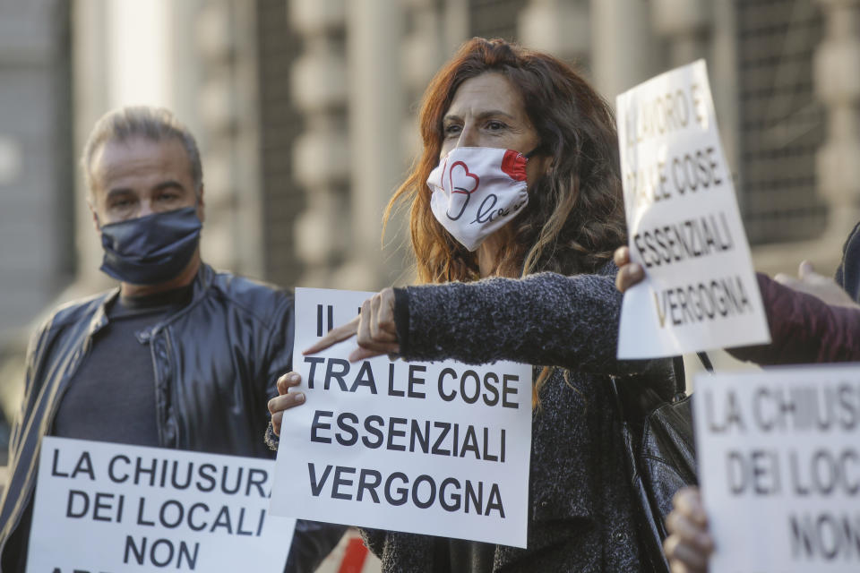 Restaurants and bars owners and dealers hold signs reading in Italian "Work is between essential things, shame on you" as they stage a protest against the government restriction measures to curb the spread of COVID-19, in front of the Milan city hall, Italy, Tuesday, Oct. 27, 2020. Italy's leader has imposed at least a month of new restrictions to fight rising coronavirus infections, shutting down gyms, pools and movie theaters and putting an early curfew on cafes and restaurants. (AP Photo/Luca Bruno)