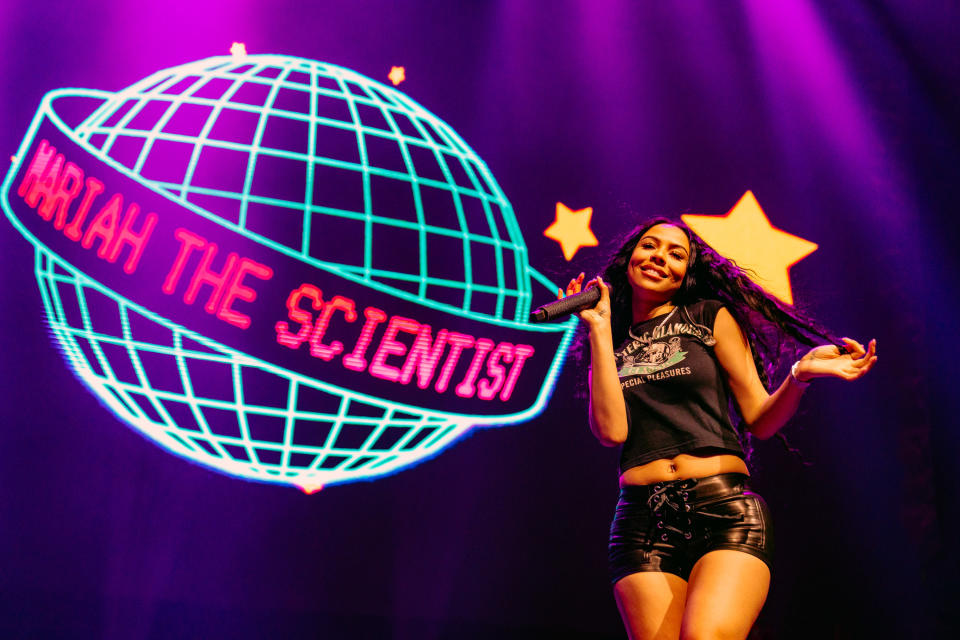 Mariah The Scientist performing on stage with a backdrop that features her stage name wrapped around a planet next to several stars