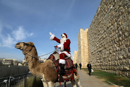 Israeli-Arab Issa Kassissieh rides a camel wearing a Santa Claus costume during the annual Christmas tree distribution by the Jerusalem municipality in Jerusalem's Old City December 21, 2017. REUTERS/Ammar Awad