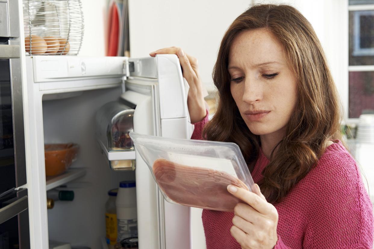 concerned woman looking at pre packaged meat from refrigerator