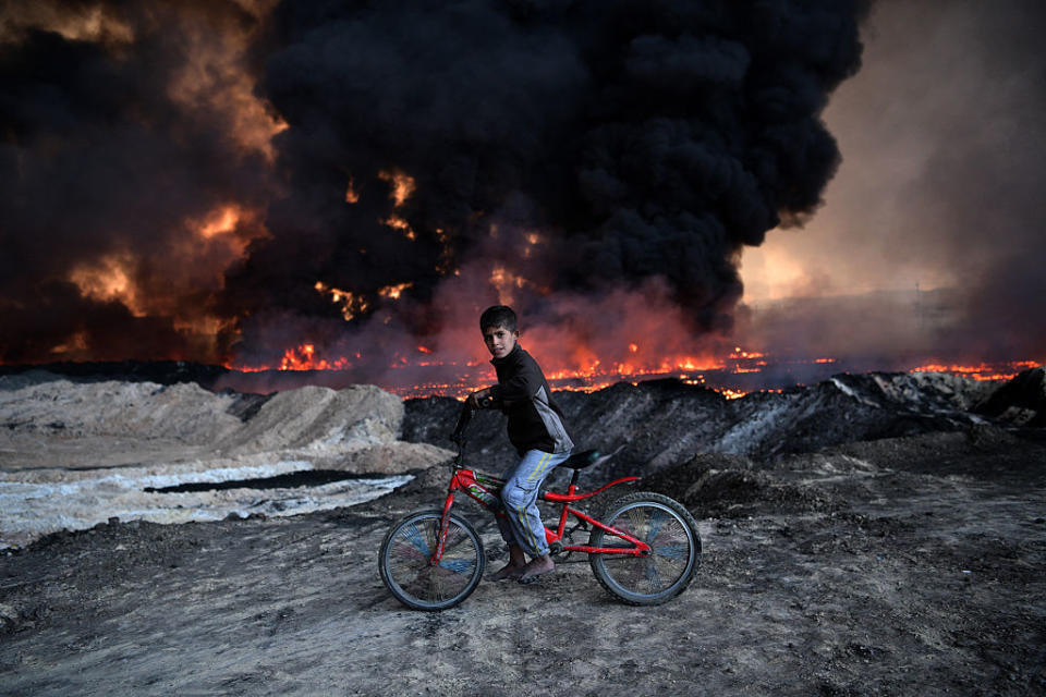 <p>A boy pauses on his bicycle as he passes an oil field that was set on fire by retreating ISIS fighters ahead of the Mosul offensive in Qayyarah, Iraq. (Carl Court/Getty Images) </p>