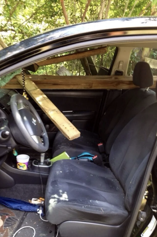 A wooden beam impales a car's windshield and front seat, with debris on the dashboard