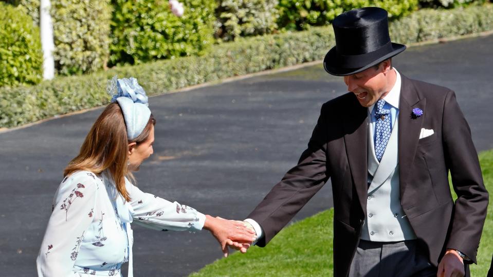 Prince William, Prince of Wales assists Carole Middleton as she gets the heel of her shoe stuck in the grass