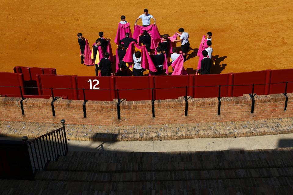 A teacher shows students how to hold capotes during bullfight master class for schoolchildren at Maestranza bullring in Andalusian capital of Seville