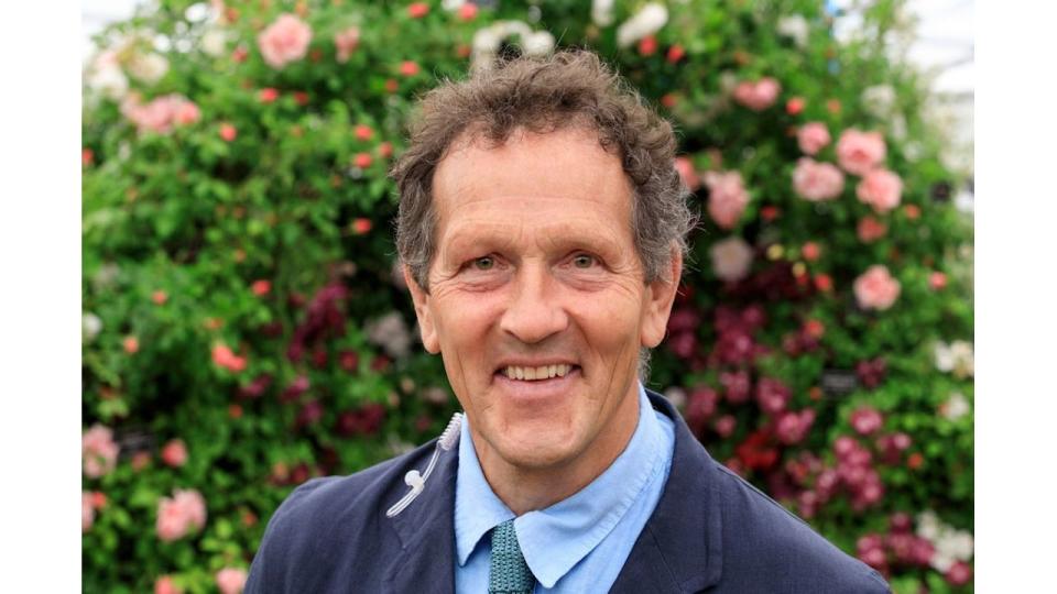 Monty Don smiling in a suit in front of a floral wall