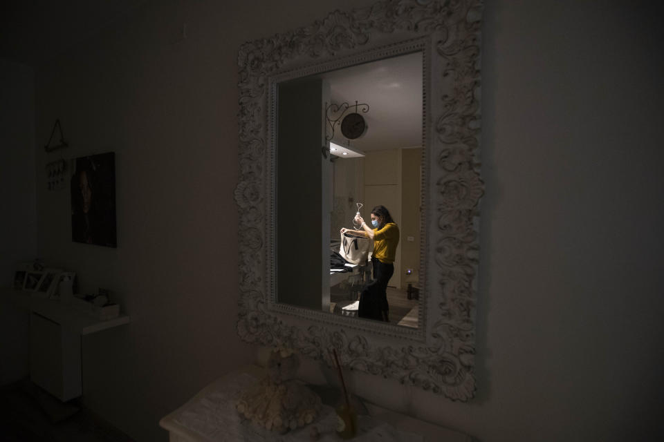 In this photo taken on Friday, April 10, 2020 nurse Cristina Settembrese is reflected in a mirror in her apartment in Basiglio, Italy as she prepares for her work shift in Milan's San Paolo Hospital. Settembrese spends her days caring for COVID-19 patients in a hospital ward, and when she goes home, her personal isolation begins by her own choice. (AP Photo/Luca Bruno)