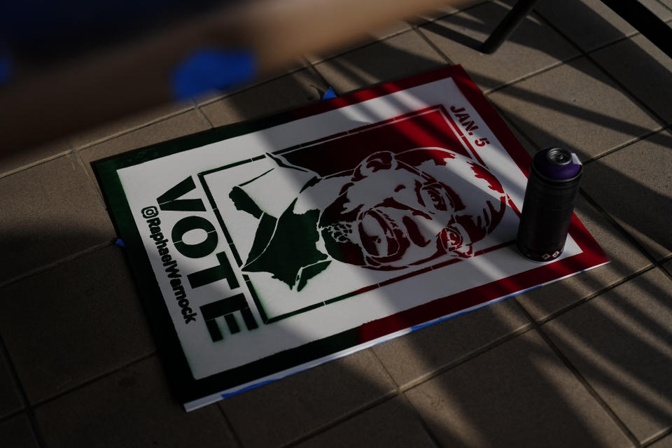 A campaign poster sits on the ground near where artist Brandon Litman, 39, of Brooklyn, N.Y., spray paints more posters after Georgia's Senate runoff race on Saturday, Jan. 9, 2021, in Atlanta. (AP Photo/Brynn Anderson)