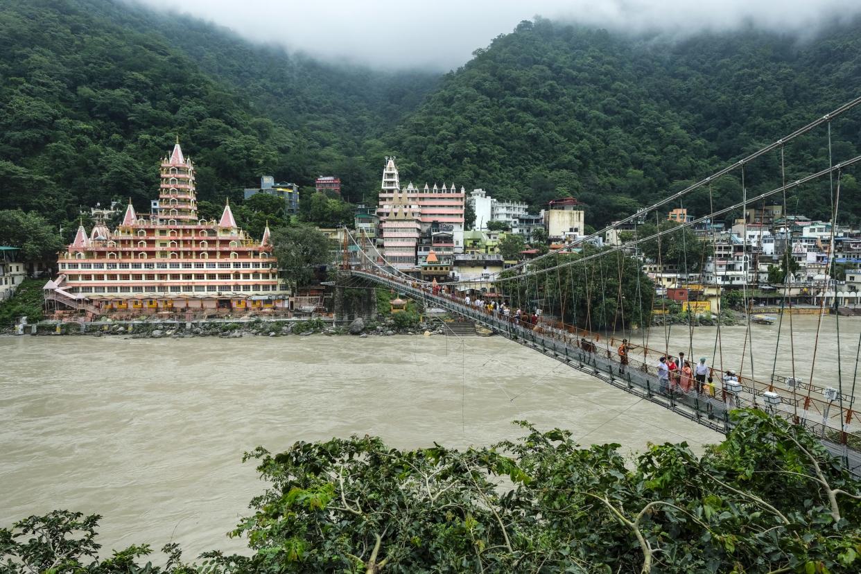 Rishikesh, India - July 2021: People passing by the Lakshman Jhula Bridge next to the Swarg Niwas Temple in Rishikesh on July 20, 2021 in Uttarakhand, India.