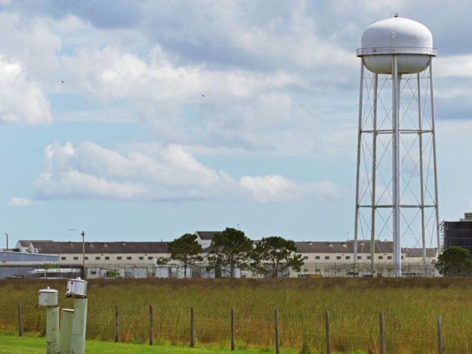 A field of grass in the foreground and a water tower and a Florida prison in the background