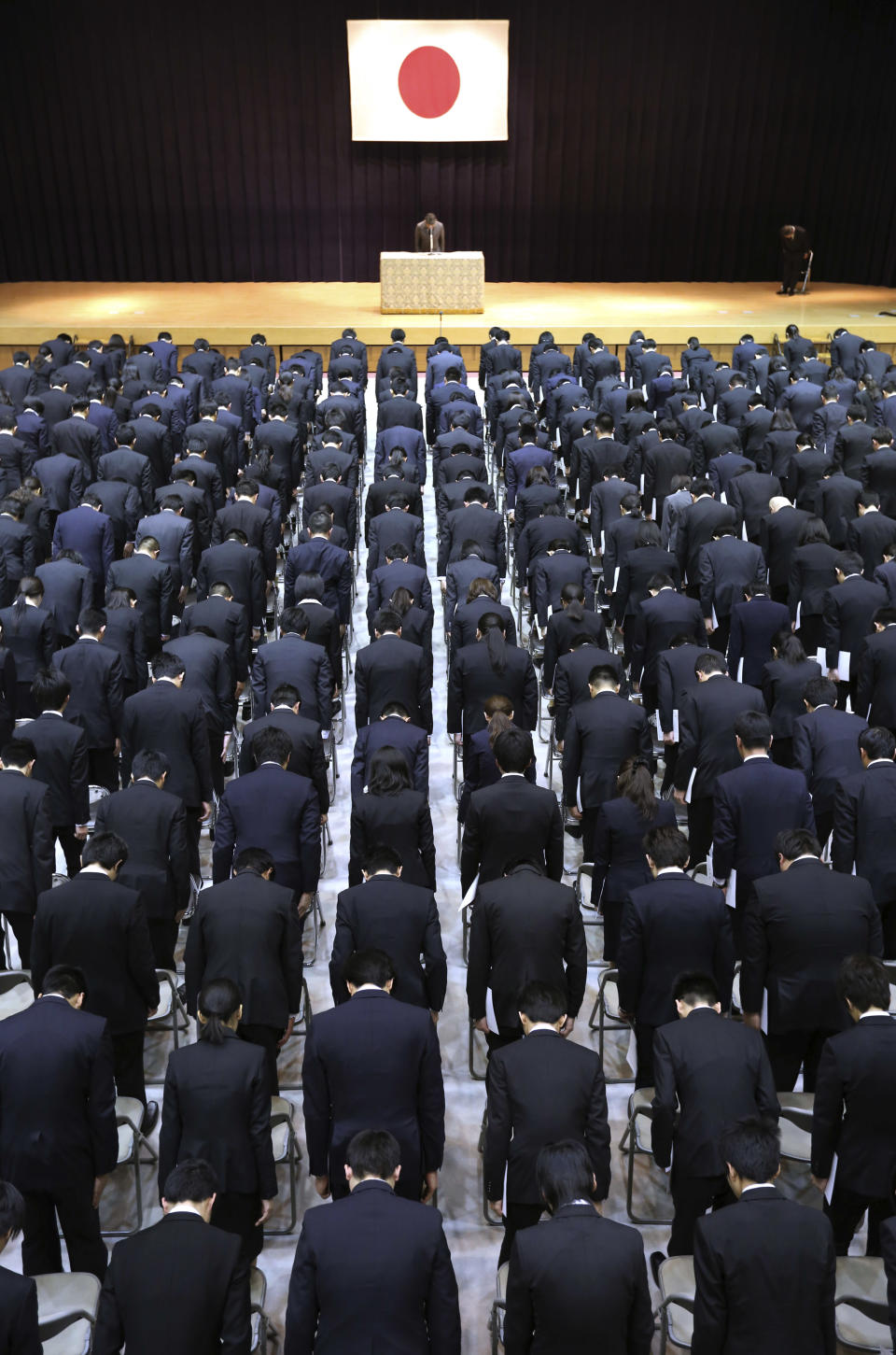 Japanese Parliamentary Senior Vice-Minister of Defense Ryota Takeda, top, and new workers bow during a welcome ceremony at Defense Ministry in Tokyo, Tuesday, April 1, 2014. Japan relaxed a decades-old ban on military-related exports Tuesday in a bid to expand joint arms development with allies and equipment sales to Southeast Asia and elsewhere. (AP Photo/Eugene Hoshiko)