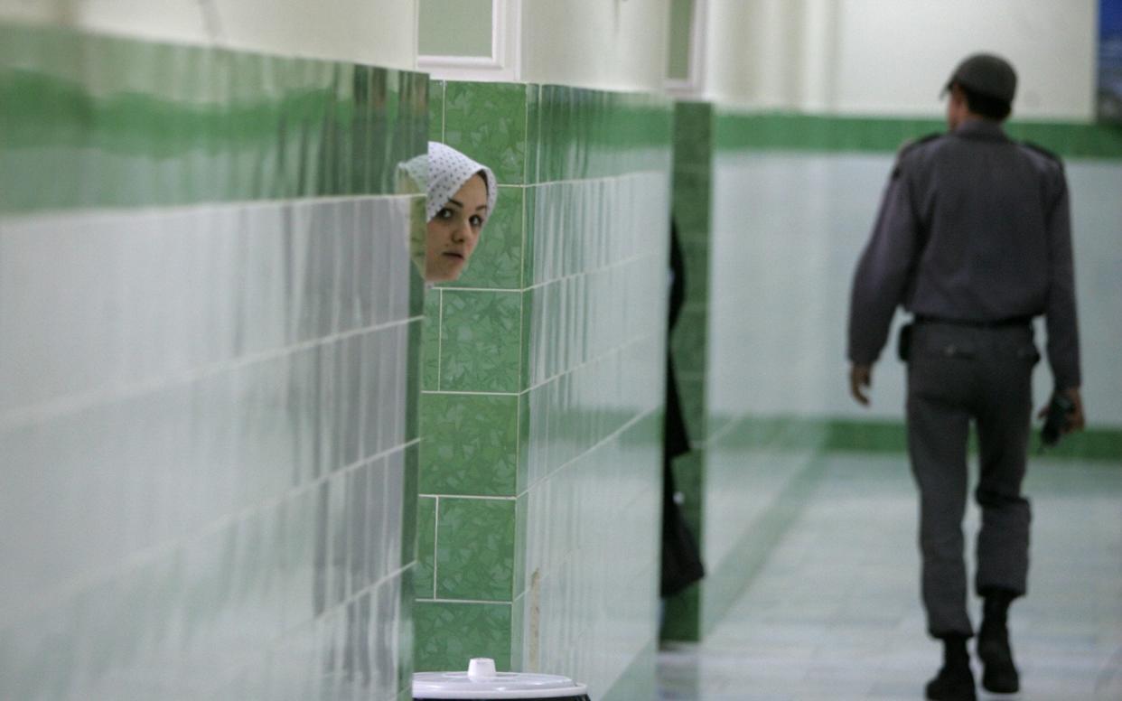 An Iranian inmate peers from behind a wall as a guard walks by at the female section of the infamous Evin jail - AFP