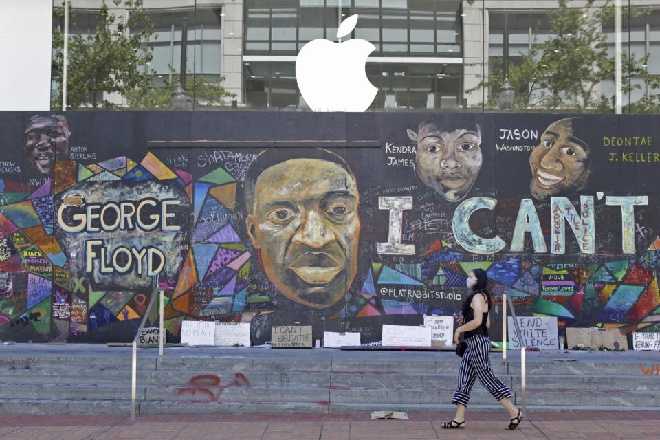 A pedestrian walks past a boarded-up Apple store that's been covered in street art in downtown Portland, Ore., Monday, July 13, 2020. While most demonstrations in the city have been peaceful, nightly violent clashes between police and protesters have divided Portland, paralyzed the downtown and attracted the attention of President Donald Trump, who sent federal law enforcement to the city to quell the unrest. (AP Photo/Gillian Flaccus)